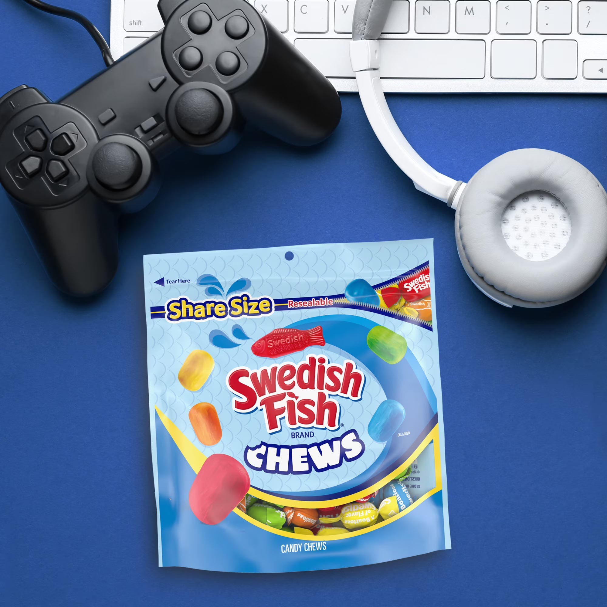 Swedish Fish Chews package with gaming controller, keyboard, and headphones on a blue background