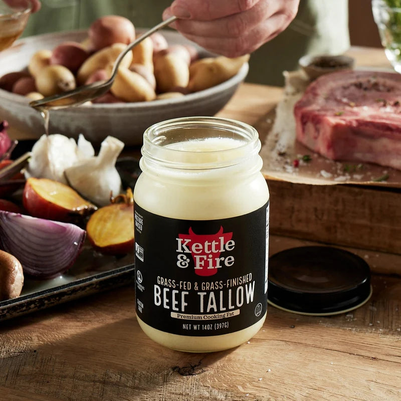 Kettle & Fire Beef Tallow jar on a wooden table with cooking ingredients in the background